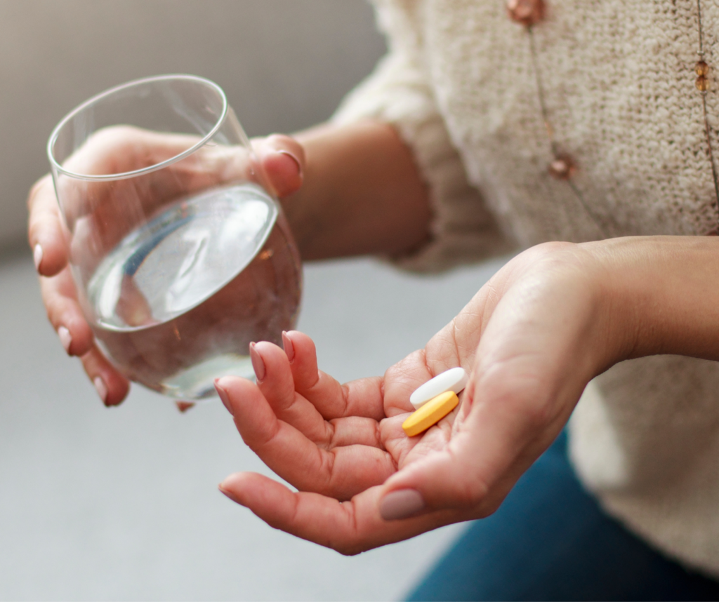 Woman holding a glass of water with a handful of vitamins in her hand. 